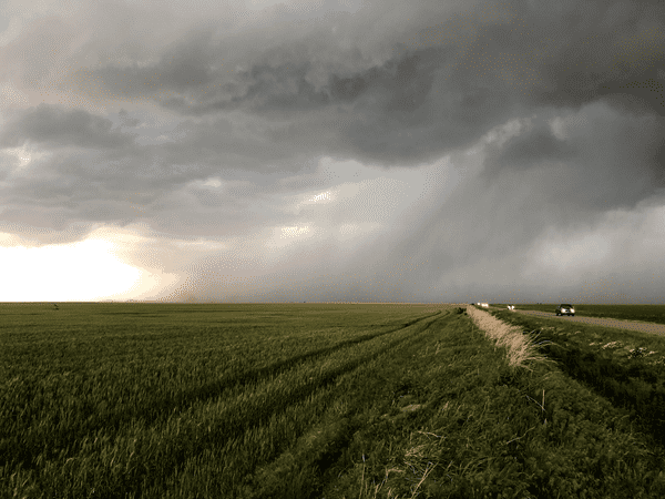 Cloudy skies over an open field by the side of the road.